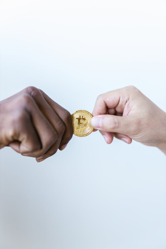 Close-up of two diverse hands exchanging a gold bitcoin coin, symbolizing cryptocurrency trade.